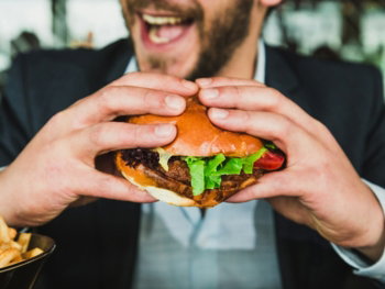 person holding burger bun with vegetables and meat